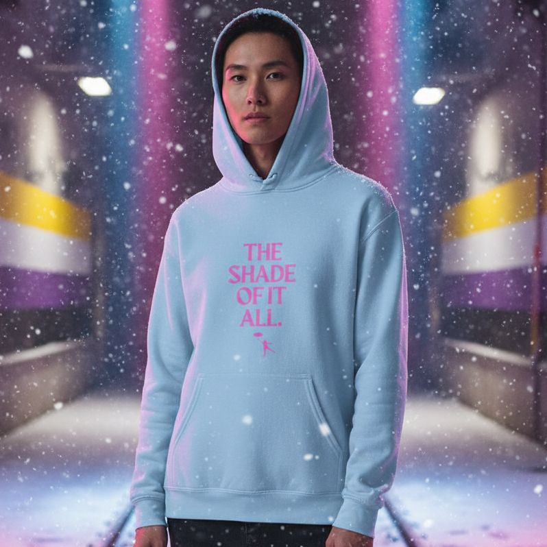 Young person in a light-blue THE SHADE OF IT ALL Unisex Hoodie stands in a moody, snow-filled corridor, exuding bold queer energy and self-expression.