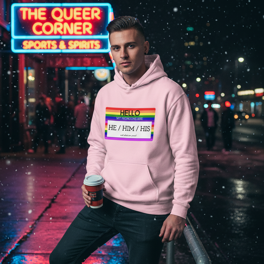Model wearing a pink pronoun hoodie with a rainbow-bordered “HE / HIM / HIS” chest graphic