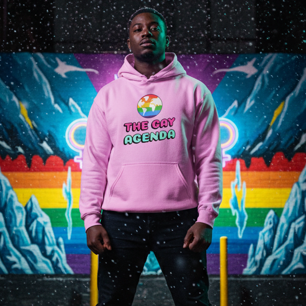 Young man wearing The Gay Agenda Unisex Hoodie with a stylized globe, exuding bold, sexy, queer energy against a vibrant mural with rainbow stripes, showcasing LGBTQ+ pride and self-expression.