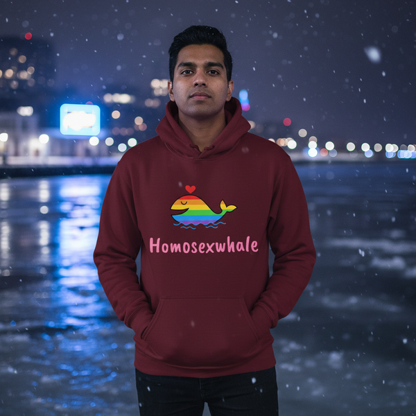 Person wearing a burgundy hoodie with a rainbow whale, heart, and “Homosexwhale” text by a snowy waterfront at night