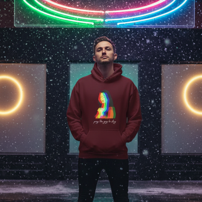 Young man in falling snow wears the Pray The Gay To Stay Unisex Hoodie with rainbow Mona Lisa print, framed by neon lights, embodying pride, empowerment, and self-expression.