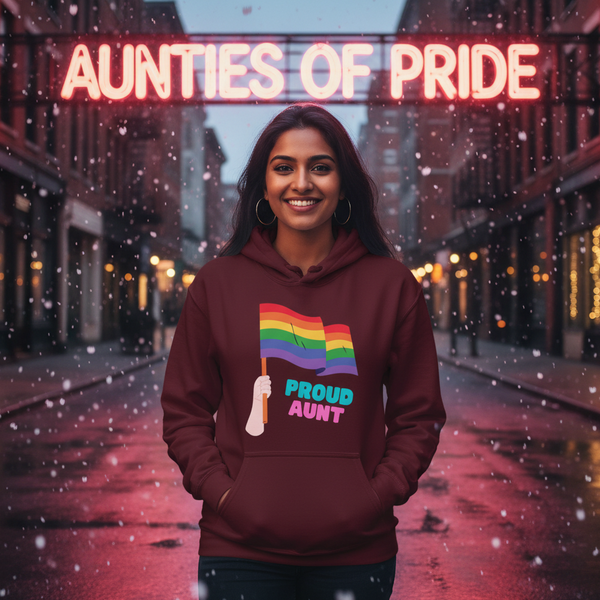 Smiling person in a burgundy hoodie with a rainbow flag and “PROUD AUNT” text, in falling snow