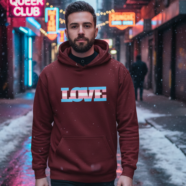Bearded person wearing a burgundy hoodie with LOVE in transgender-pride stripes in a snowy neon-lit alley