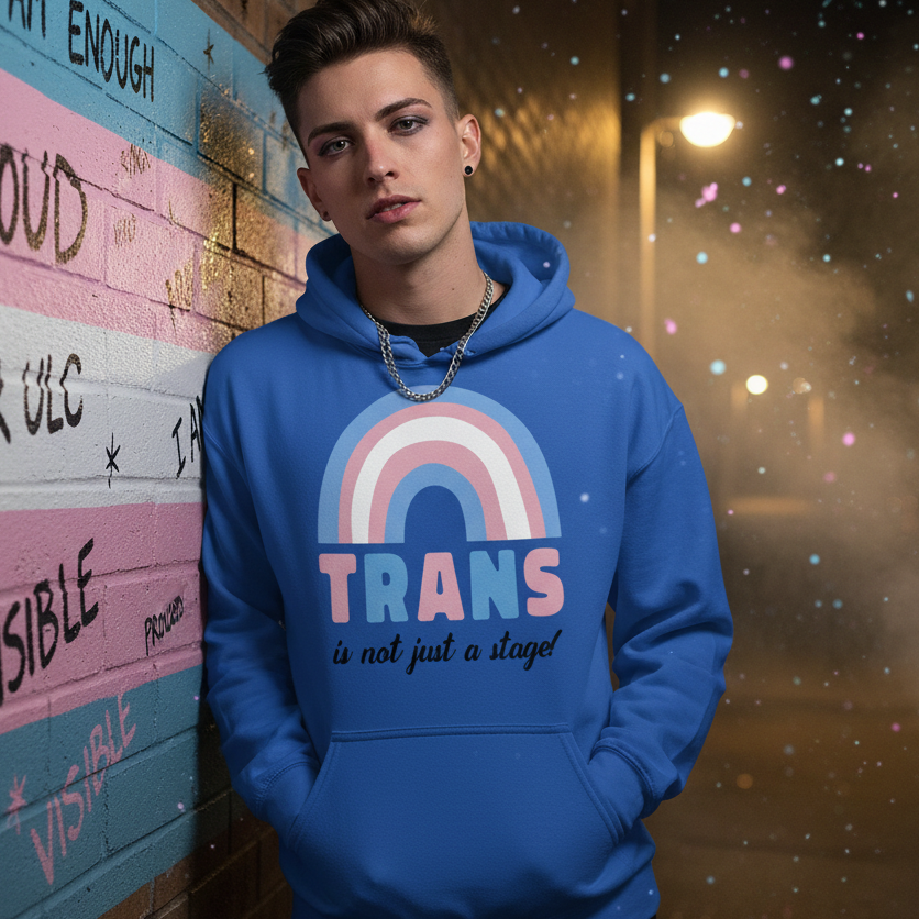 A young person models the Trans Is Not Just A Stage! Unisex Hoodie, featuring trans-flag colors and empowering slogan, symbolizing queer pride and self-expression against an affirming, urban backdrop.