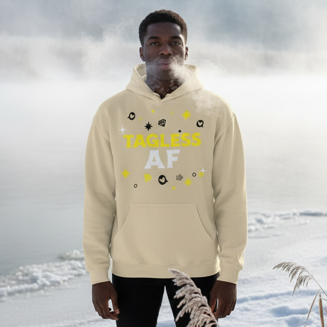 Young man in a misty outdoor setting wears a light-cream Tagless AF Unisex Hoodie, featuring bold yellow and white text with abstract icons, embodying queer pride and self-expression.
