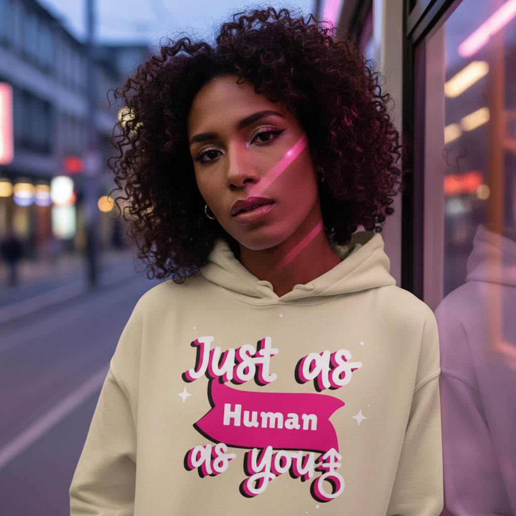 Young person in a Just As Human As You Unisex Hoodie, leaning against a glass surface with pink neon light, embodying pride and self-expression.