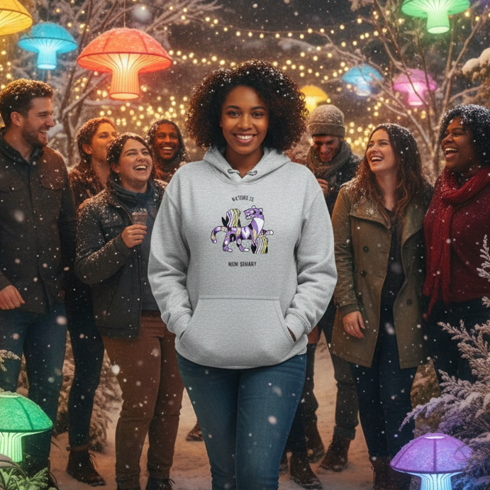 A young Black woman smiles warmly in a light gray Nature Is Non-Binary Unisex Hoodie, featuring abstract animal graphics in vibrant hues, embodying queer pride and self-expression amidst a festive, snowy backdrop.