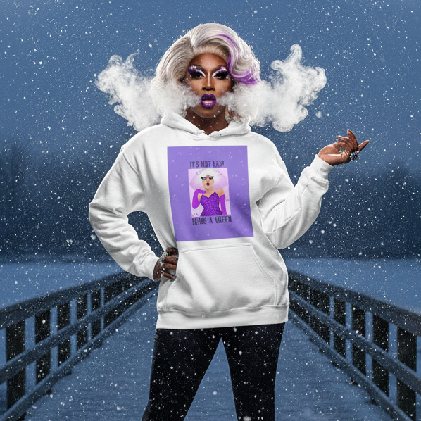 Drag performer in a platinum-blonde wig models the It's Not Easy Being a Queen Unisex Hoodie on a snowy boardwalk, showcasing its bold graphic and cozy style, exuding prideful, queer confidence.