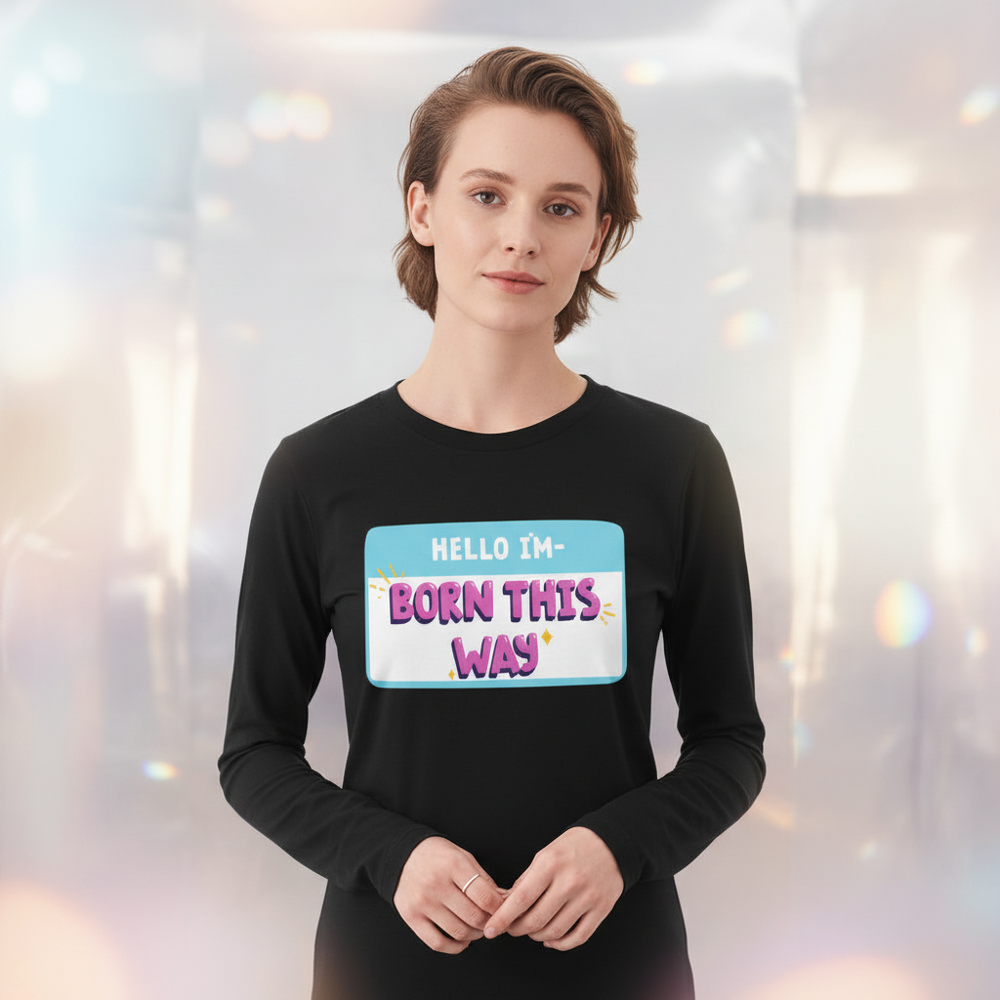 Unisex long sleeve tee with a bold, colorful "HELLO IM BORN THIS WAY" nametag; model has short light brown hair.
