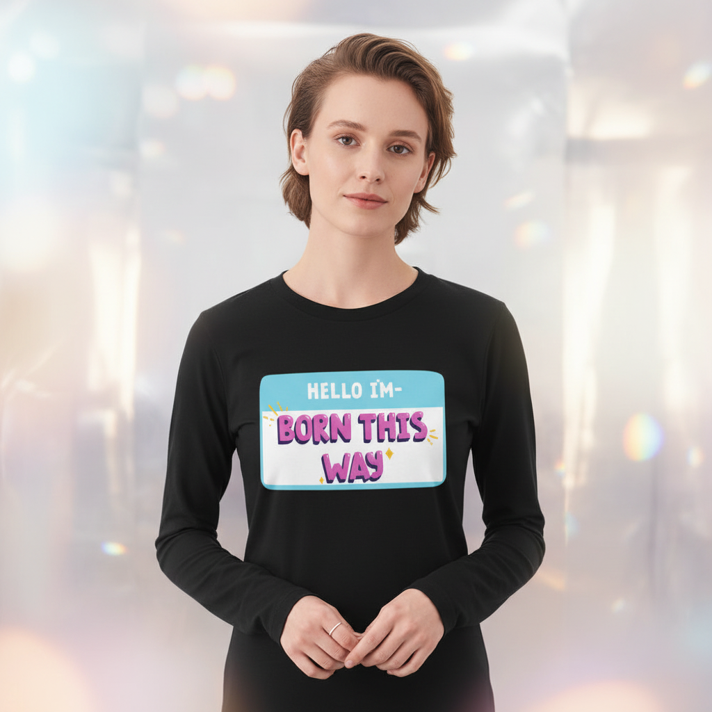 Unisex long sleeve tee with a bold, colorful "HELLO IM BORN THIS WAY" nametag; model has short light brown hair.