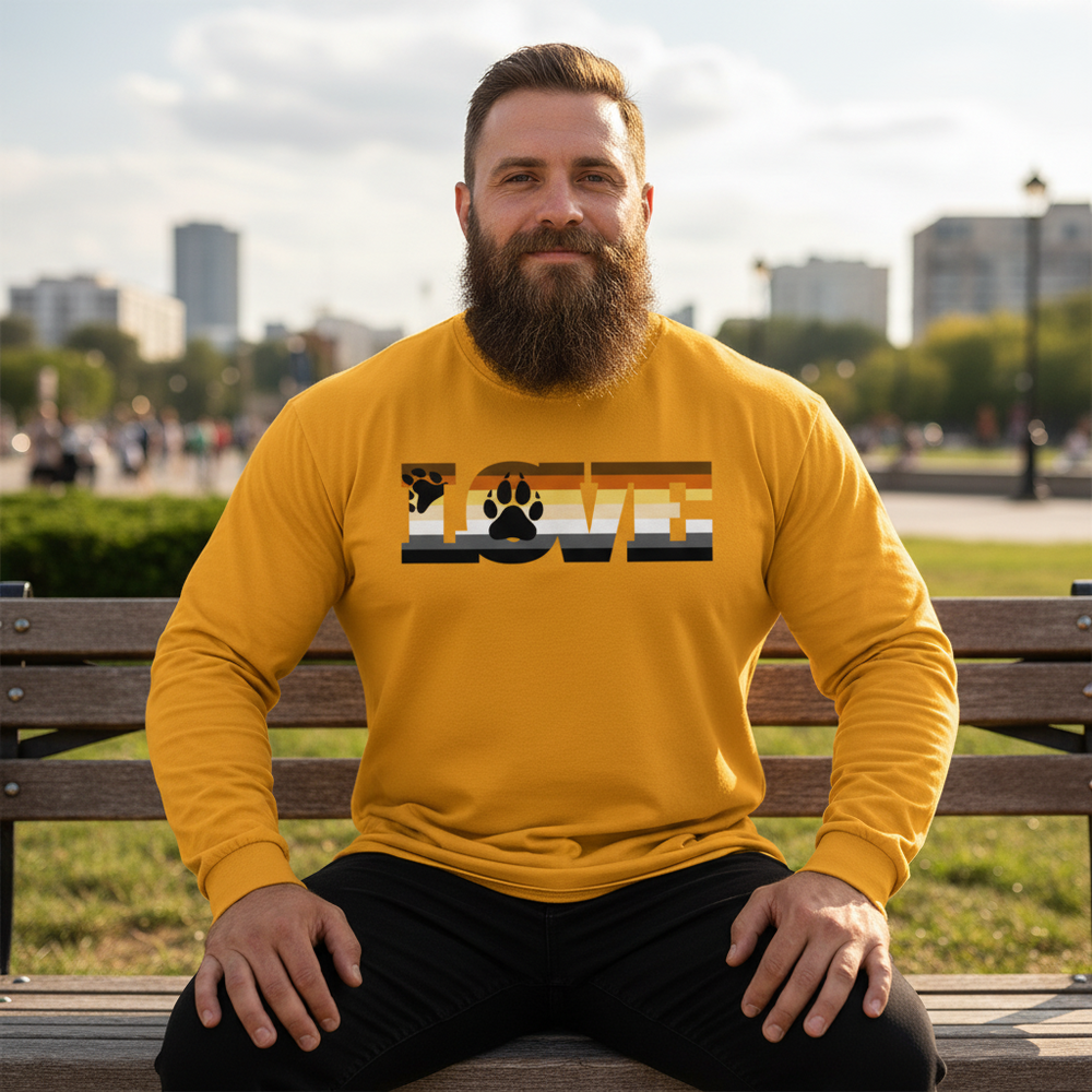 Gay Bear Pride long sleeve tee with "LOVE" in Bear flag colors and paw prints, worn by a bearded man on a city park bench.