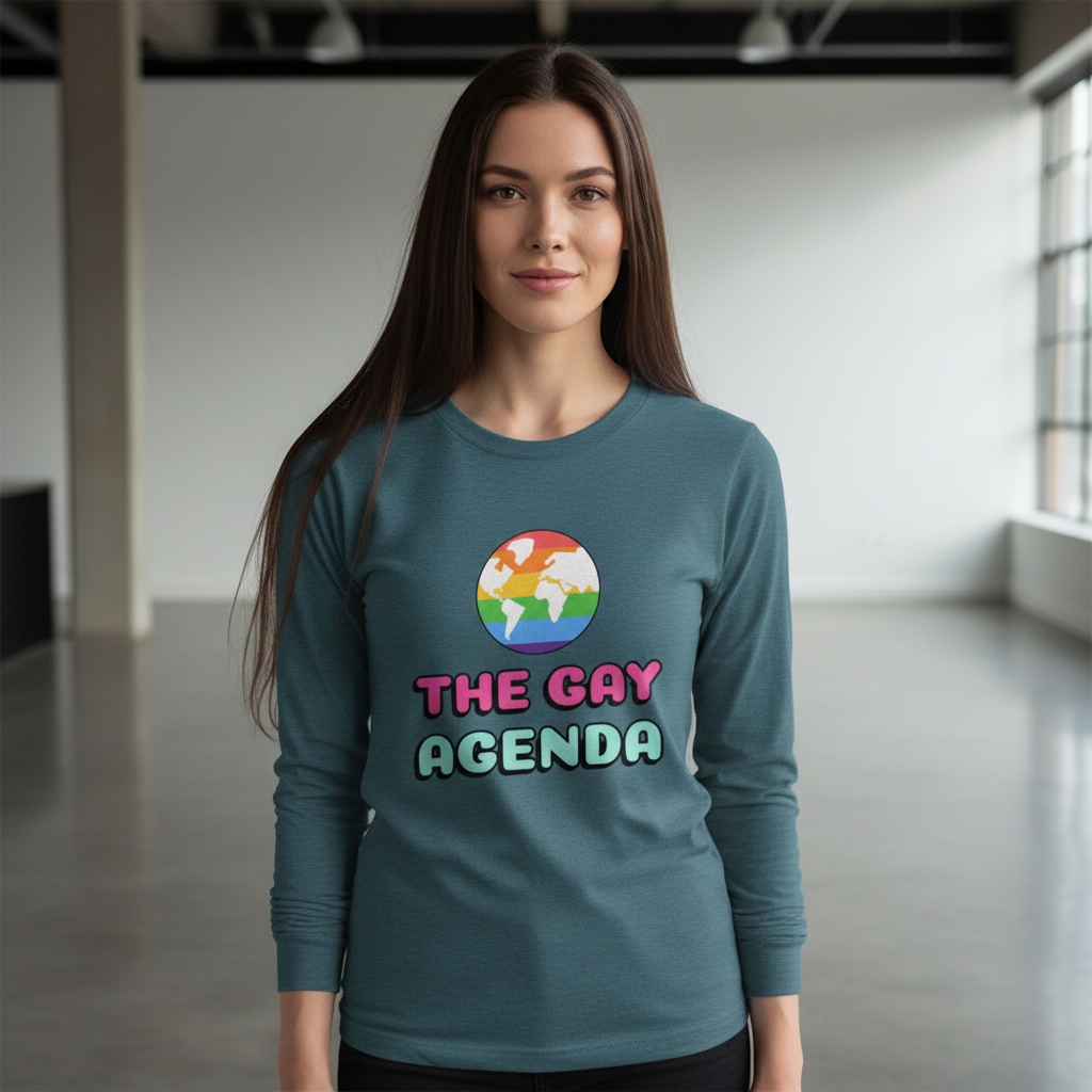 Young woman wearing The Gay Agenda Unisex Long Sleeve T-Shirt featuring a rainbow-striped globe and bold text, embodying pride and self-expression in a light-filled room with exposed beams.
