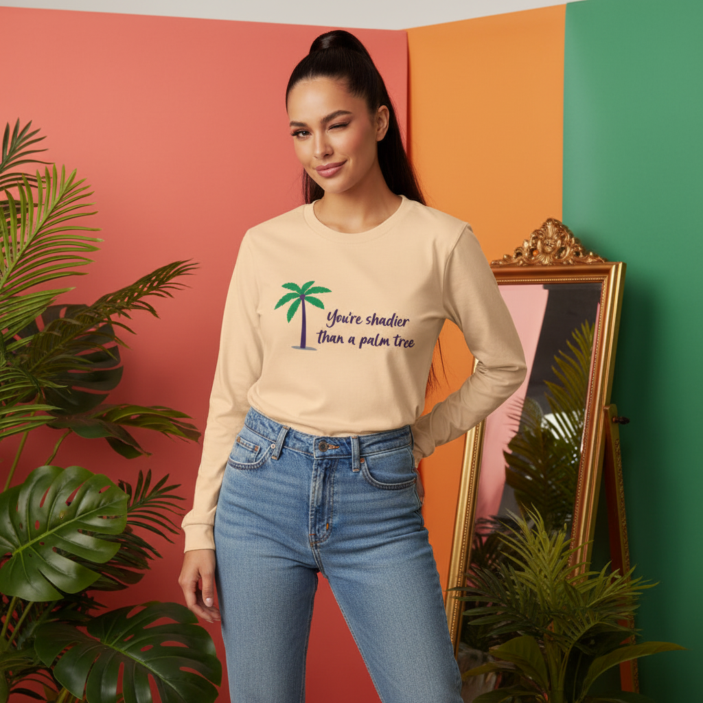 Young woman in light-blue jeans and a pale-yellow Shadier Than A Palm Tree Unisex Long Sleeve T-Shirt, playfully winking amidst tropical plants, embodying vibrant, queer pride and self-expression.