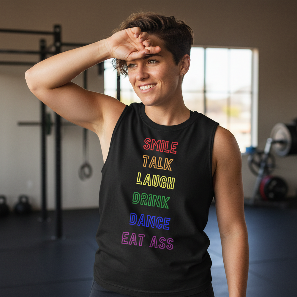Black unisex muscle tee with "Smile, Talk, Laugh, Drink, Dance, Eat Ass" in rainbow text; queer person at gym raising hand.