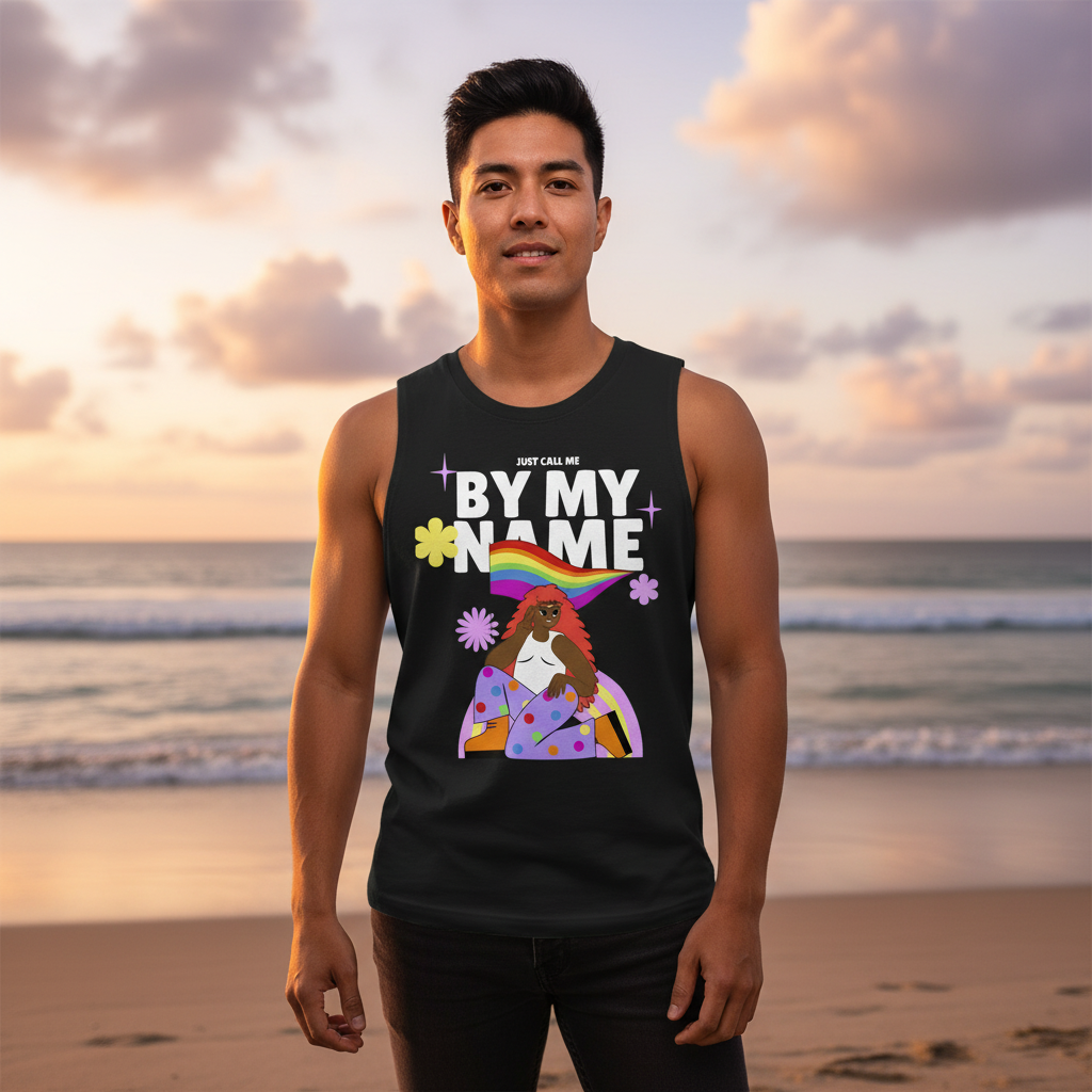 A young man stands on a beach in a Just Call Me By My Name Muscle Tank, featuring a vibrant illustration celebrating queer pride and self-expression against a sunset backdrop.