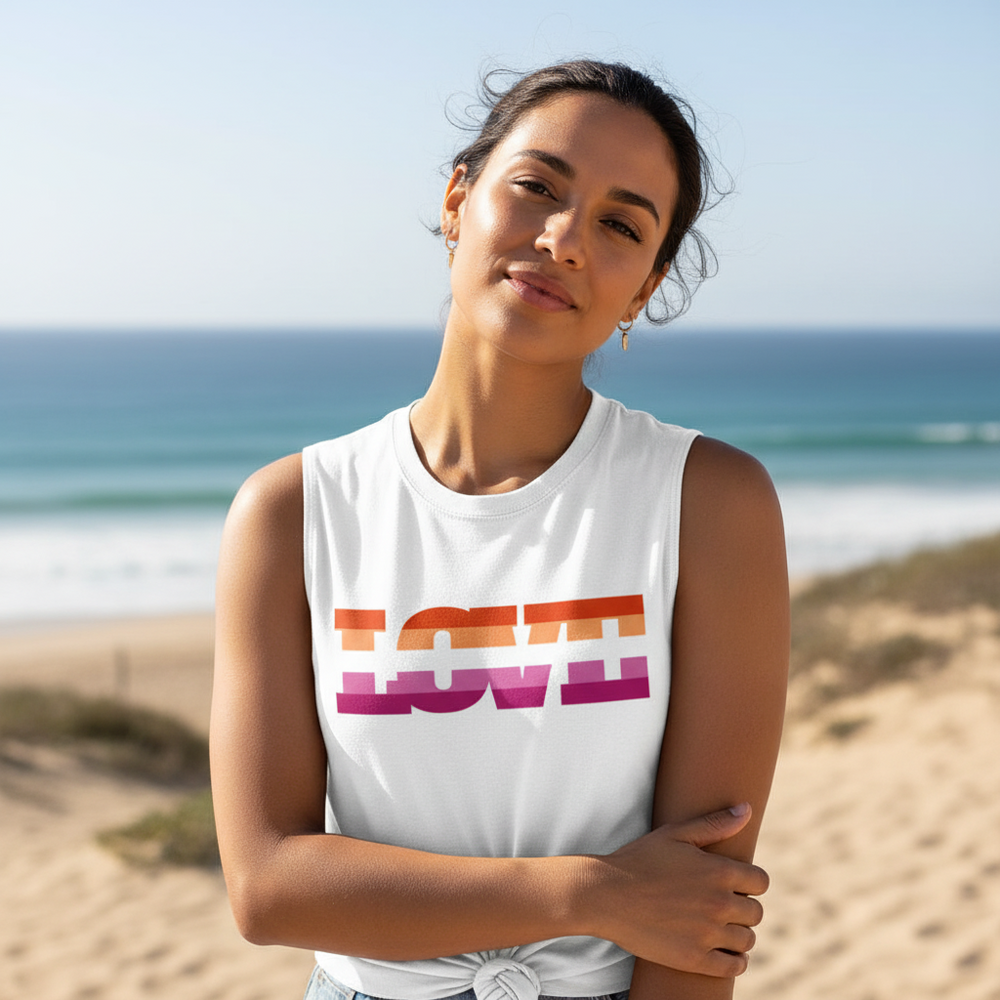Lesbian Love Muscle Top, sleeveless with bold, colorful "LOVE" stripes, relaxed fit; woman stands on beach, arms crossed.