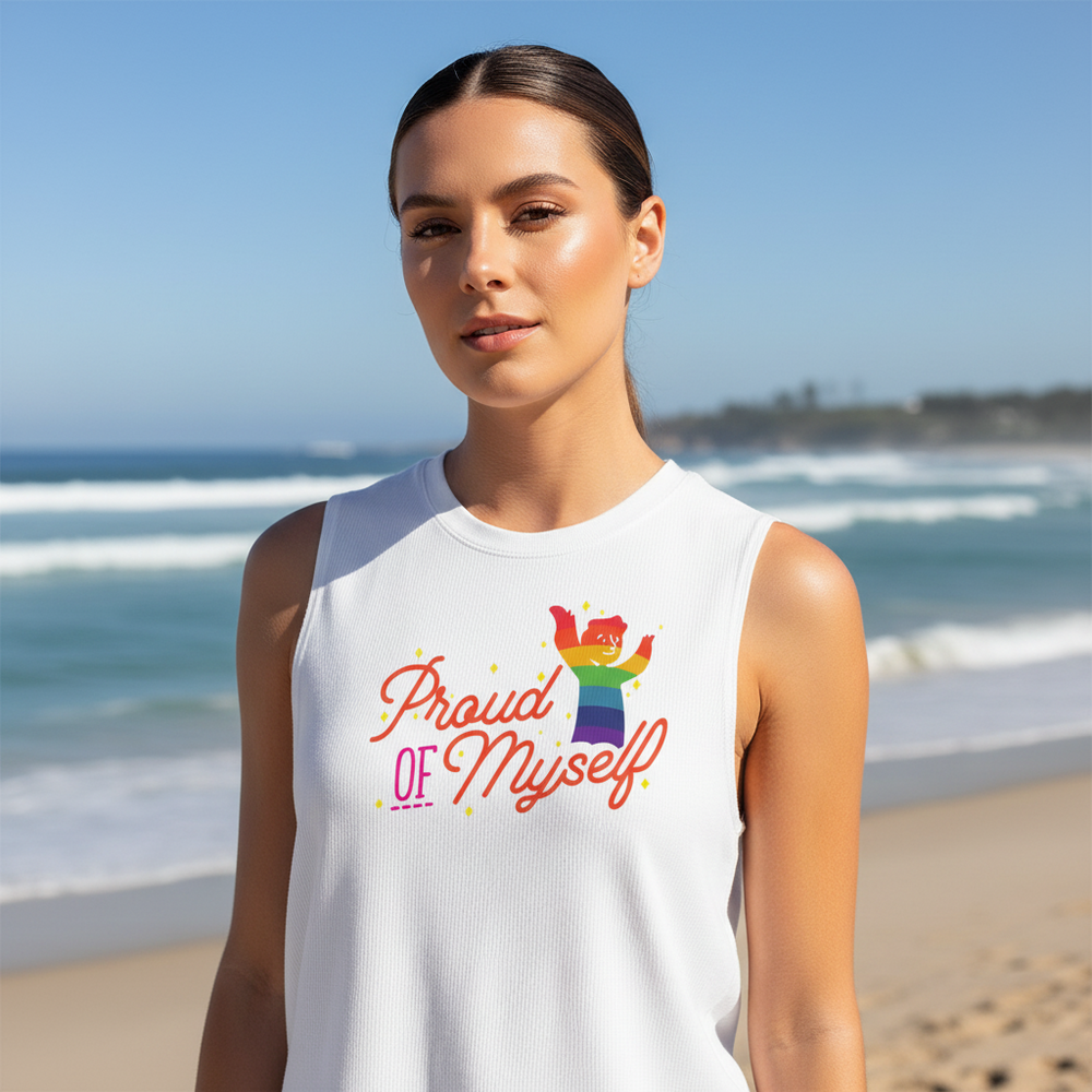 Proud Of Myself Muscle Top with a rainbow “Proud of Myself!” and vivid cartoon art, worn by a woman on a sunny queer beach.