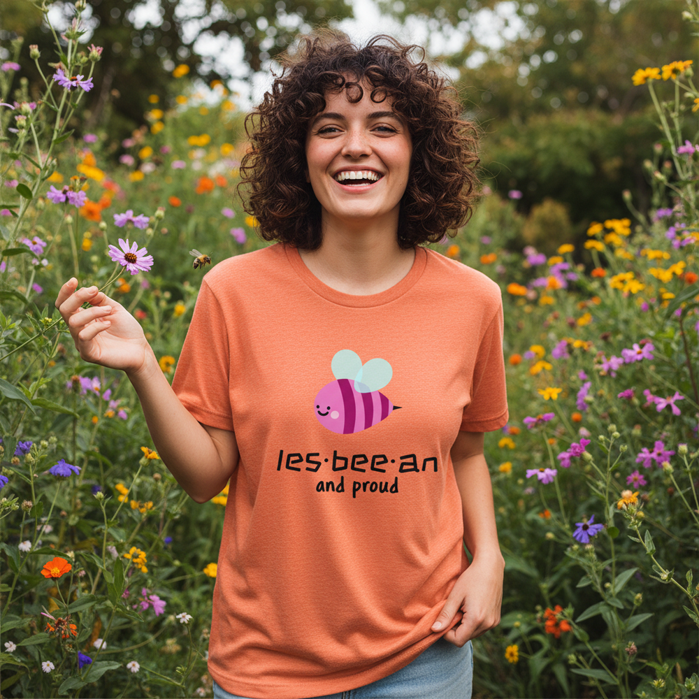 Smiling model in a flower meadow wears an orange T-shirt with a bee and “les-bee-an and proud”