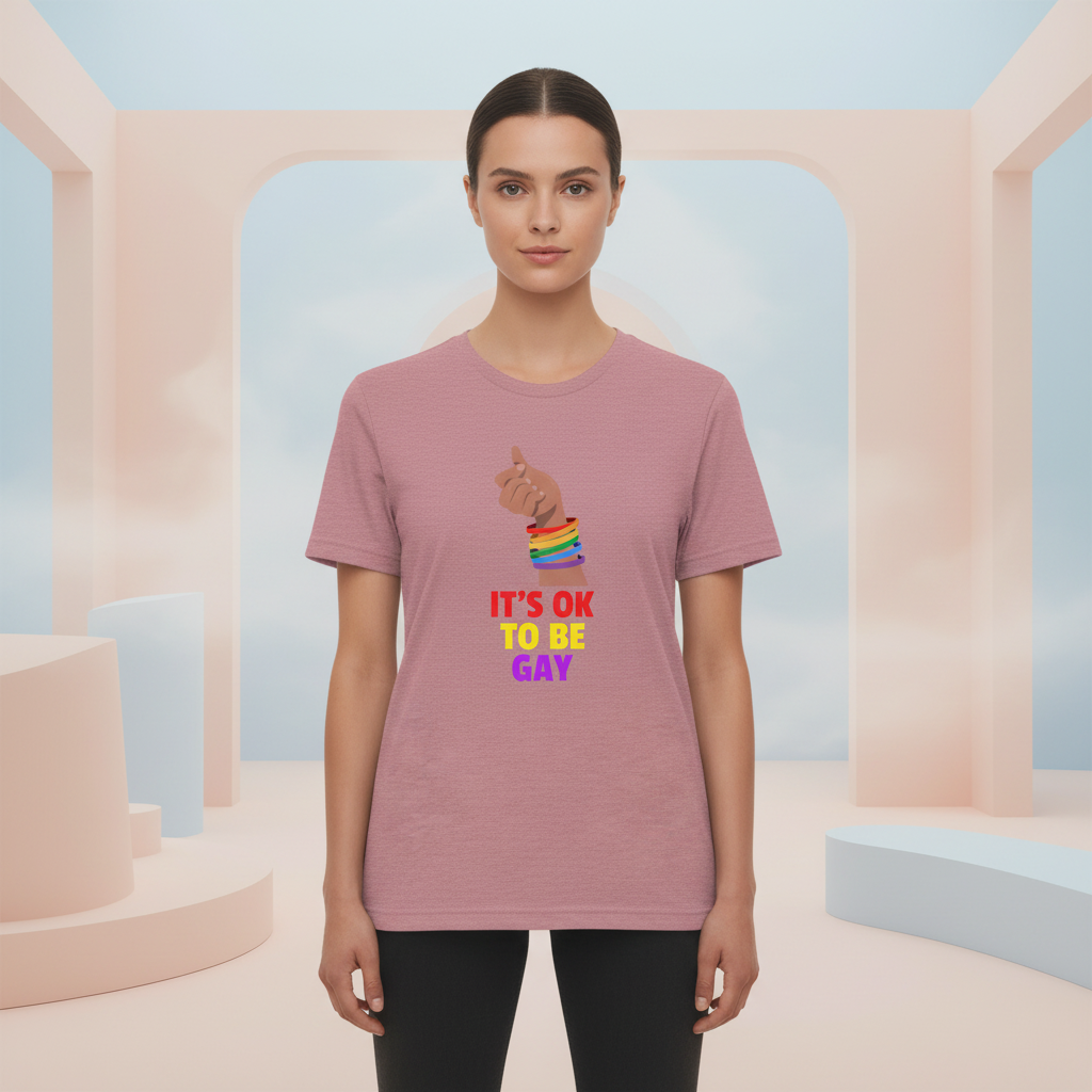 It's OK To Be Gay T-shirt with rainbow fist and bold pride text, worn by a woman in pastel space, queer style, facing forward.