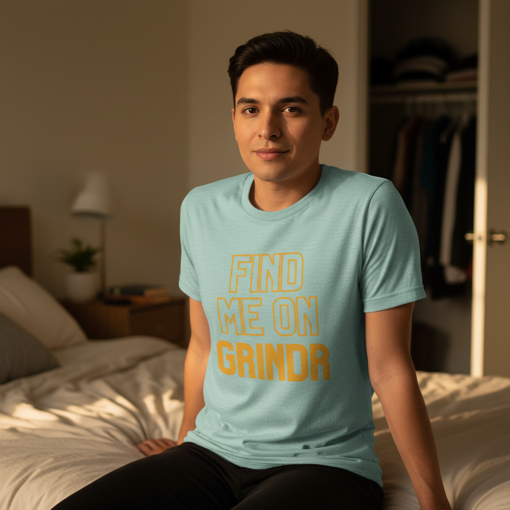 Find Me On Grindr" T-shirt worn by a young man with short dark hair, sitting on a bed in a queer-coded, softly lit room.