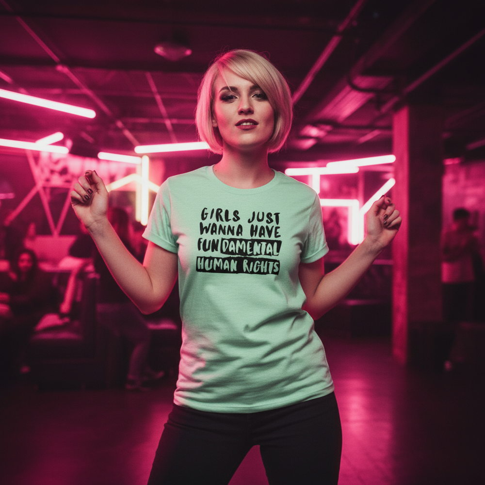 Girls Just Wanna Have Fundamental Human Rights T-shirt worn by a femme with short blonde hair in a neon-lit queer club scene.