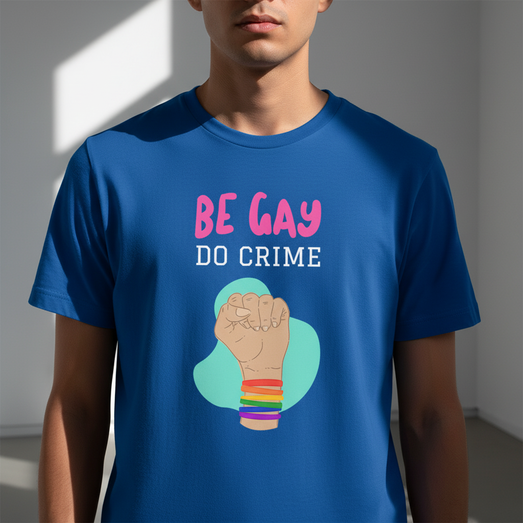 Model wearing a blue T-shirt reading “BE GAY DO CRIME” with a rainbow-bracelet fist graphic