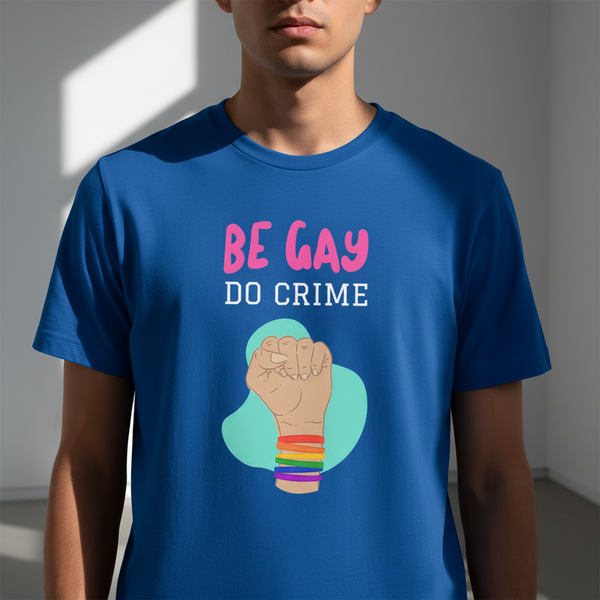 Model wearing a blue T-shirt reading “BE GAY DO CRIME” with a rainbow-bracelet fist graphic
