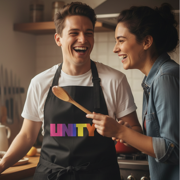 Person wearing a black apron with a multicolored UNITY print while cooking with a person