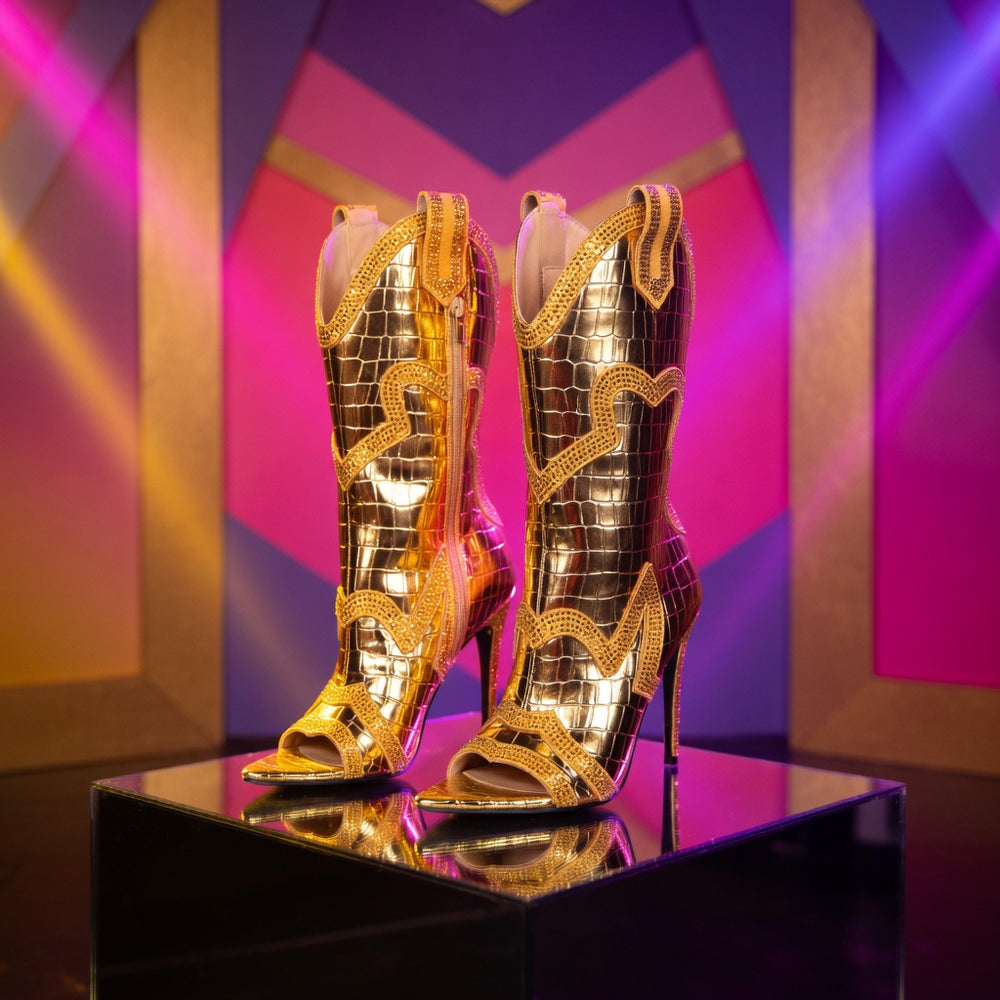 Golden croc-texture superheroine boots with open toes, high heels, wavy trim, and heart details on a mirrored platform.