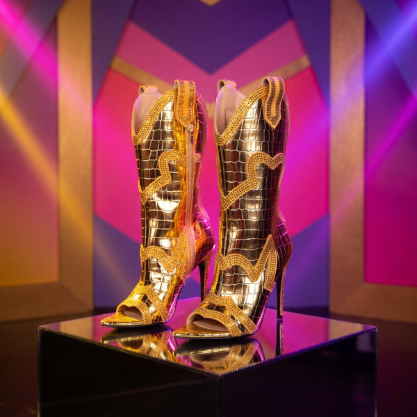 Golden croc-texture superheroine boots with open toes, high heels, wavy trim, and heart details on a mirrored platform.
