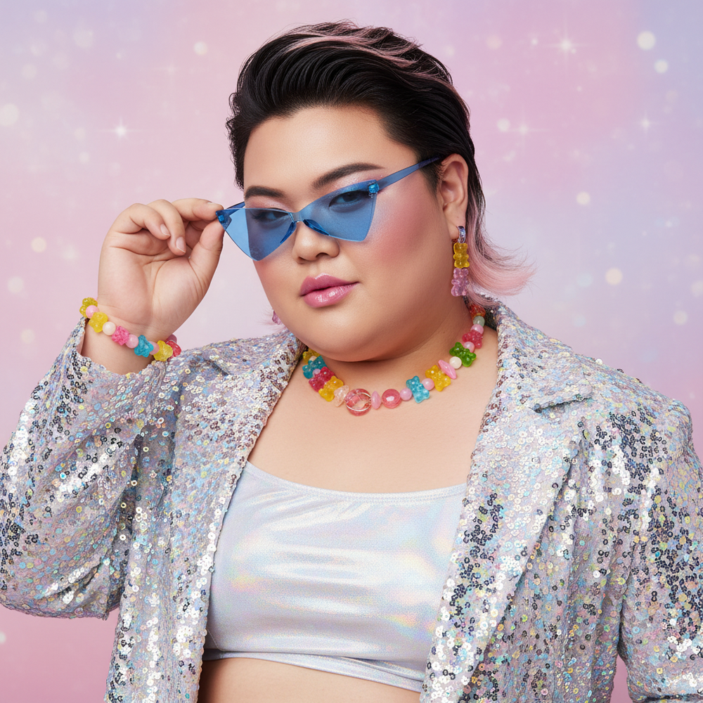 Person with short dark hair and pink highlights in Visions Of Candy Sunglasses, silver sequin jacket, crop top
