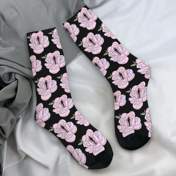 Pair of black crew socks with pink vulva-shaped floral designs, arranged on white and gray fabric