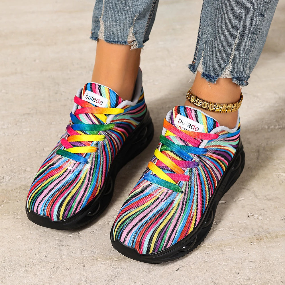 Pair of multicolored striped sneakers with rainbow laces, shown on a model's feet