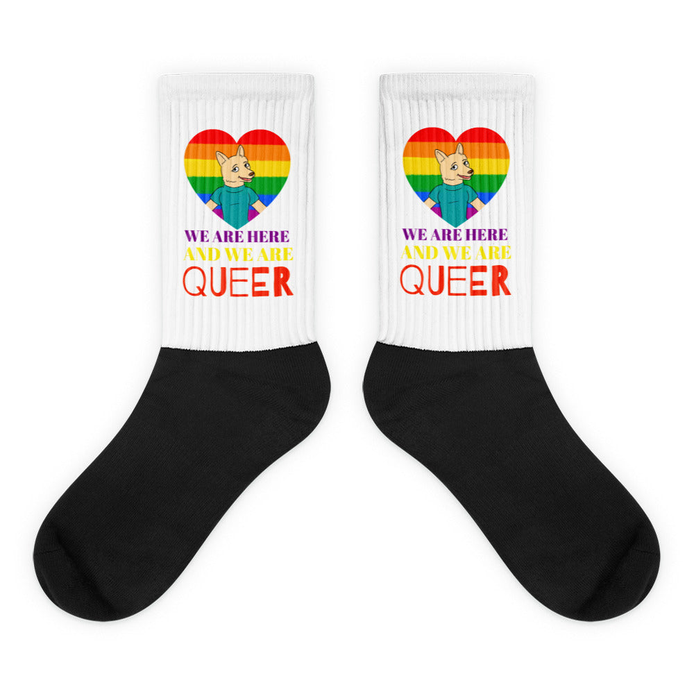 Pair of white-cuff, black-foot socks with rainbow hearts, corgi figures, and “WE ARE HERE AND WE ARE QUEER” text