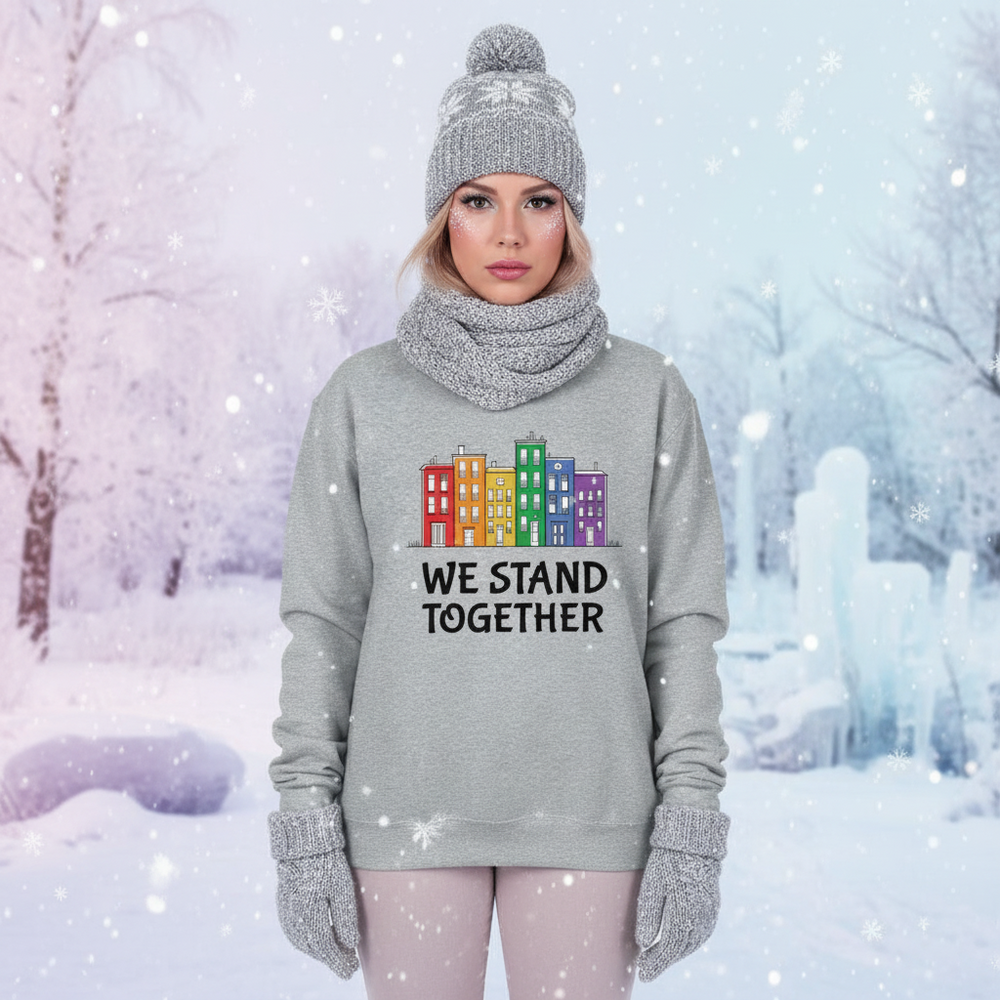 Front-facing model wears a gray sweatshirt reading “WE STAND TOGETHER” with colorful buildings in snowfall
