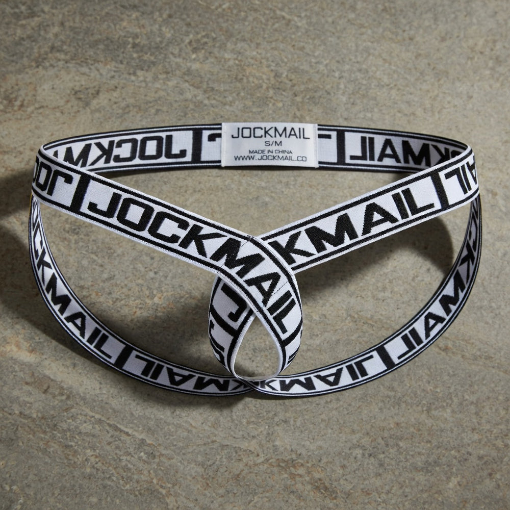 White and black Jockmail elastic cockstrap displayed unworn on warm grey stone.