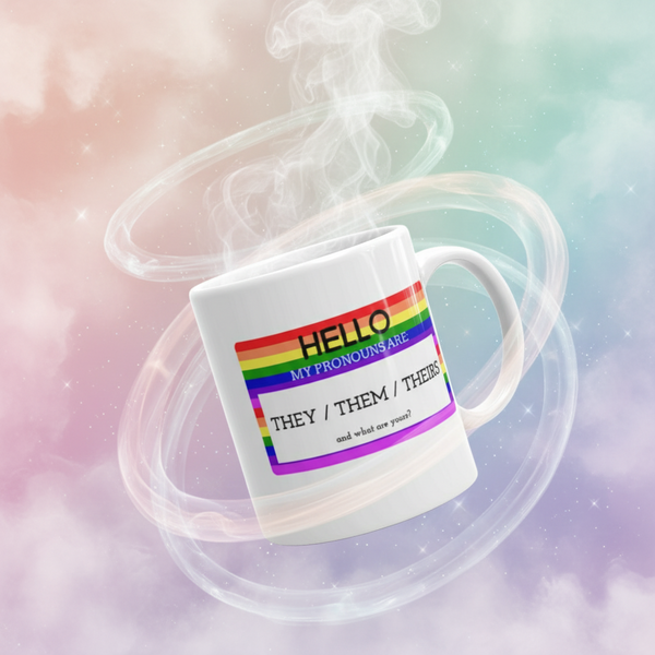 White mug with rainbow stripes reading “HELLO MY PRONOUNS ARE THEY / THEM / THEIRS”