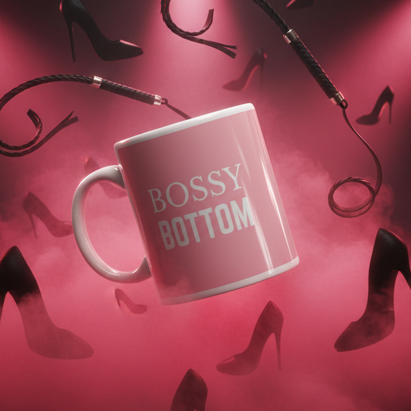 Bossy Bottom Mug suspended midair with black stiletto heels and a leather whip, embodying bold queer pride and empowerment. Perfect for coffee or wine, this ceramic mug is dishwasher and microwave safe.