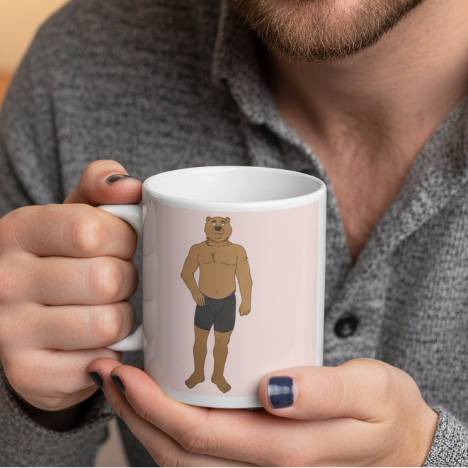Close-up of the Gay Cub Mug featuring a cartoon bear with a human body in briefs. Held by someone with dark nail polish, this sturdy, glossy mug celebrates LGBTQIA+ pride and self-expression.