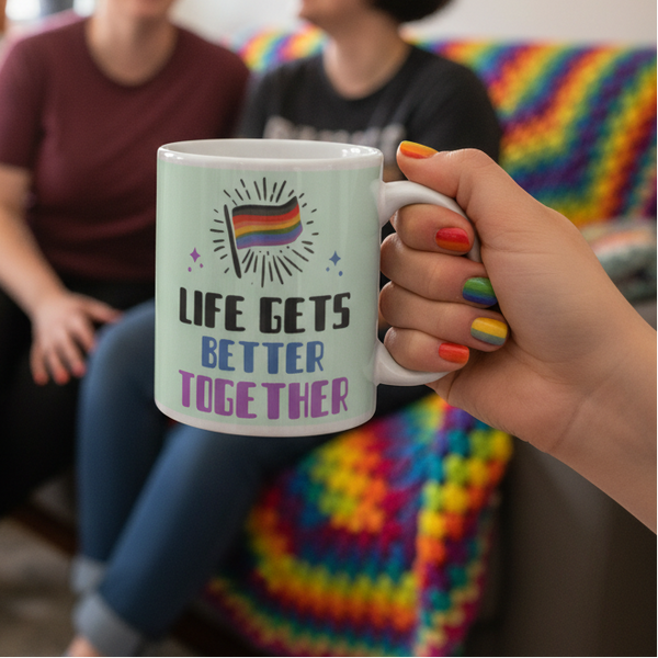 Life Gets Better Together Mug held by a hand with rainbow-painted nails, showcasing a vibrant pride message. In the background, a cozy, LGBTQ+ affirming scene with pride-themed decor enhances the joyful, inclusive atmosphere.
