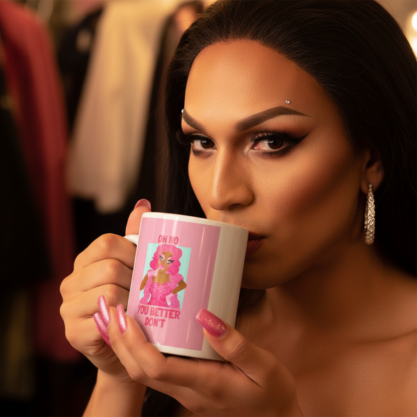 Drag performer sipping from an Oh No You Betta Don't Mug featuring a pink-haired cartoon and bold phrase. The scene embodies queer pride and self-expression, with vibrant makeup, glitter nails, and chic accessories.