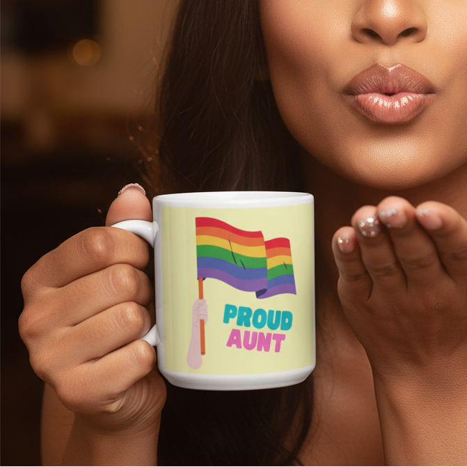 Person holds a Proud Aunt Mug, featuring a vivid illustration of a hand waving a pride flag and colorful text, embodying LGBTQIA+ pride and visibility with a softly lit, empowering gesture.