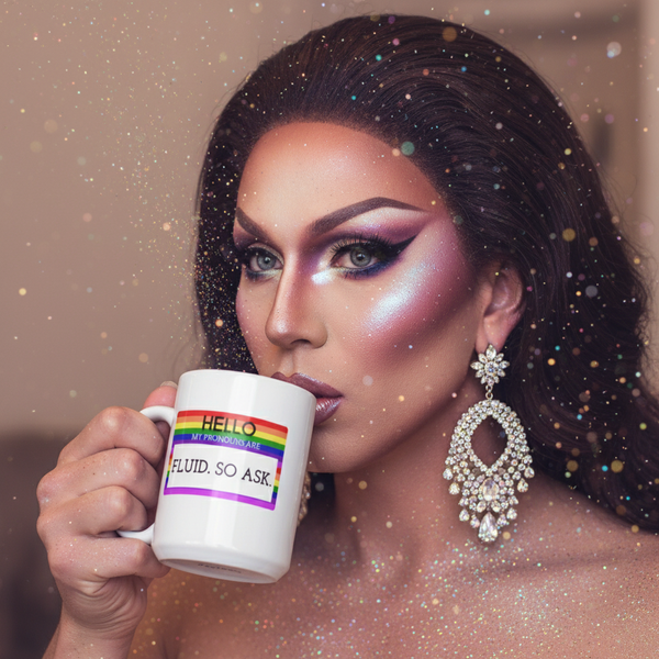 Drag performer holding a white mug reading “Hello My Pronouns Are Fluid. So Ask.”