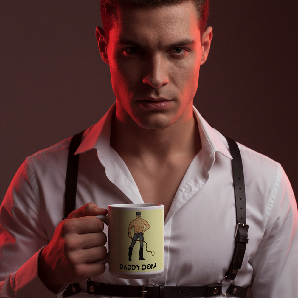 Person in a white shirt and black harness holds a mug labeled “DADDY DOM” with a cartoon figure.