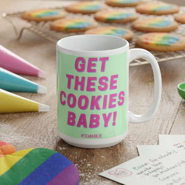 Get These Cookies Mug on a wooden countertop, featuring bold pink lettering. Perfect for prideful self-expression, surrounded by colorful icing bags and cookies, embodying Queer In The World's joyful, inclusive ethos.