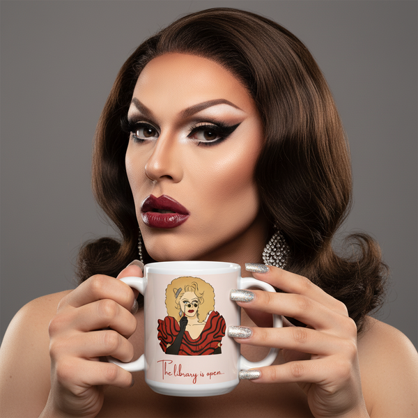 Drag performer holds a white mug showing a blonde cartoon and “The library is open...”