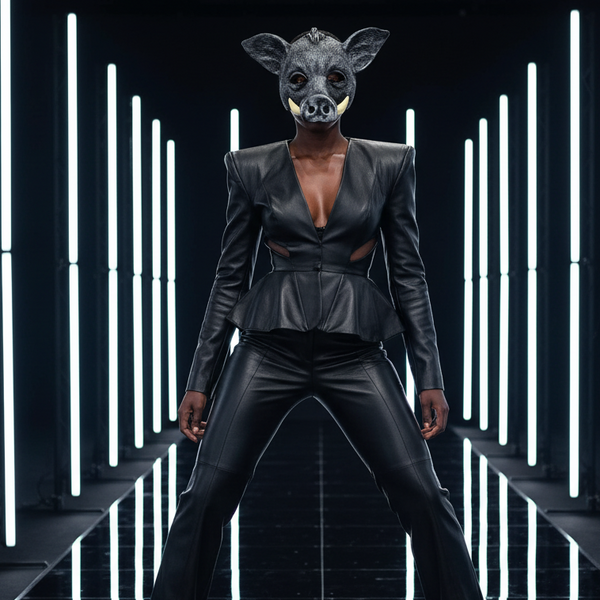 Front-facing model wearing a black pig mask, leather-look top, and pants