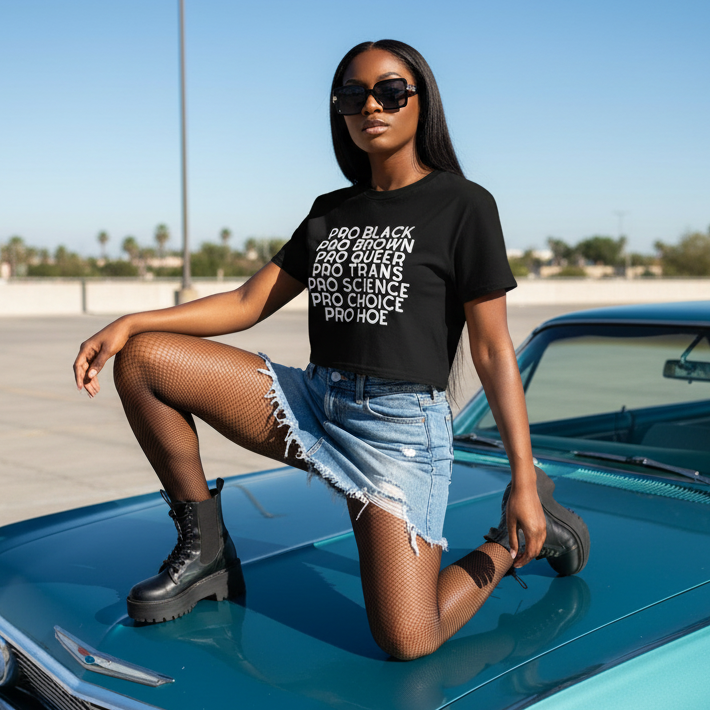 A young person confidently poses on a teal vintage car, showcasing the Pro Hoe White Crop Top, which celebrates queer identity and self-expression with empowering PRO statements, paired with a frayed denim mini-skirt.