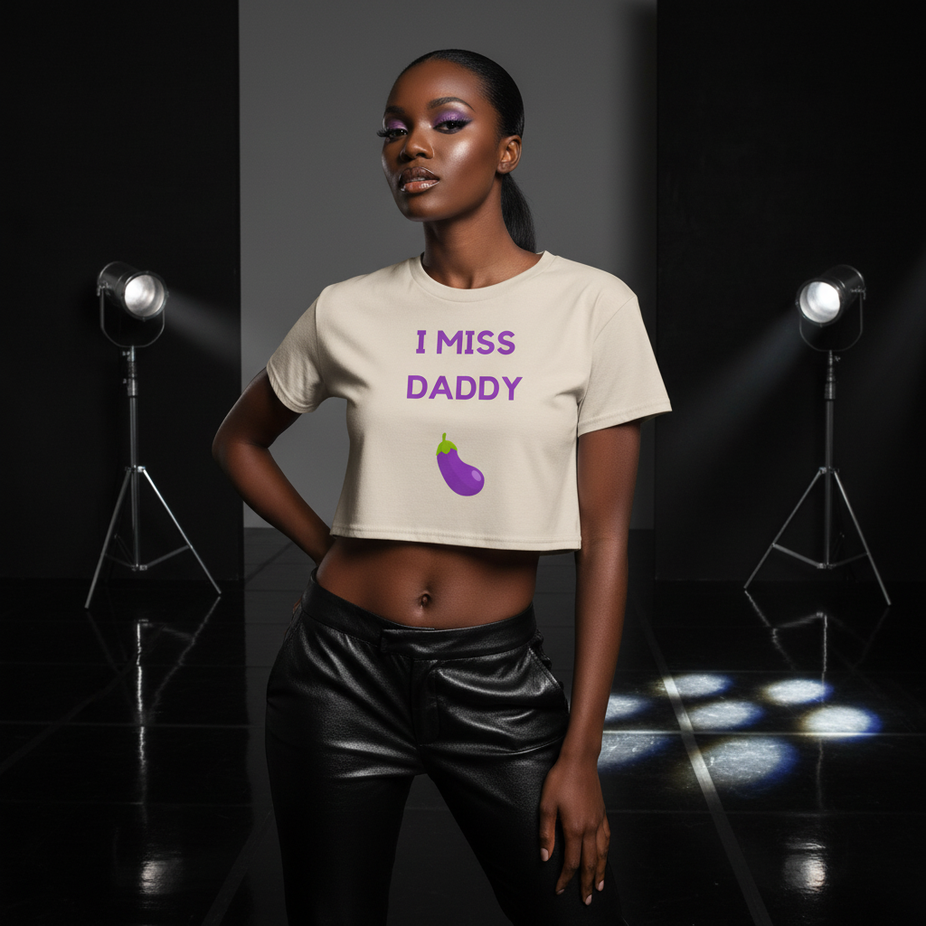 The I Miss Daddy Crop Top with an eggplant print, worn by a bold femme in black leather pants and loud makeup, under moody lights.