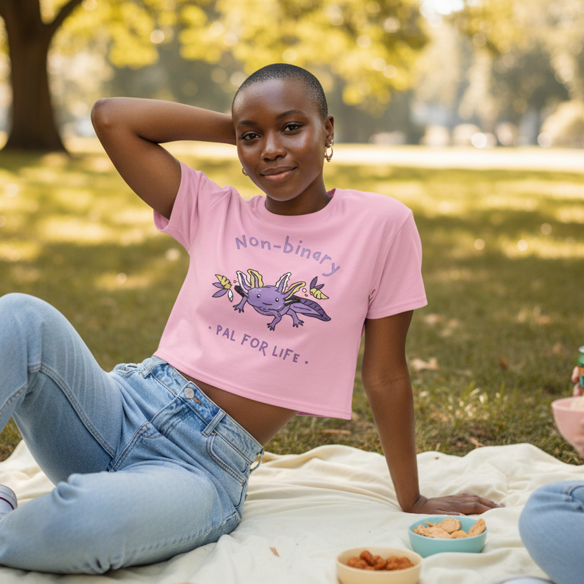 A person wearing the Non-Binary Pal For Life Crop Top relaxes on a picnic blanket, exuding queer confidence and joy with a cartoon axolotl design, surrounded by snacks in a sunlit park.
